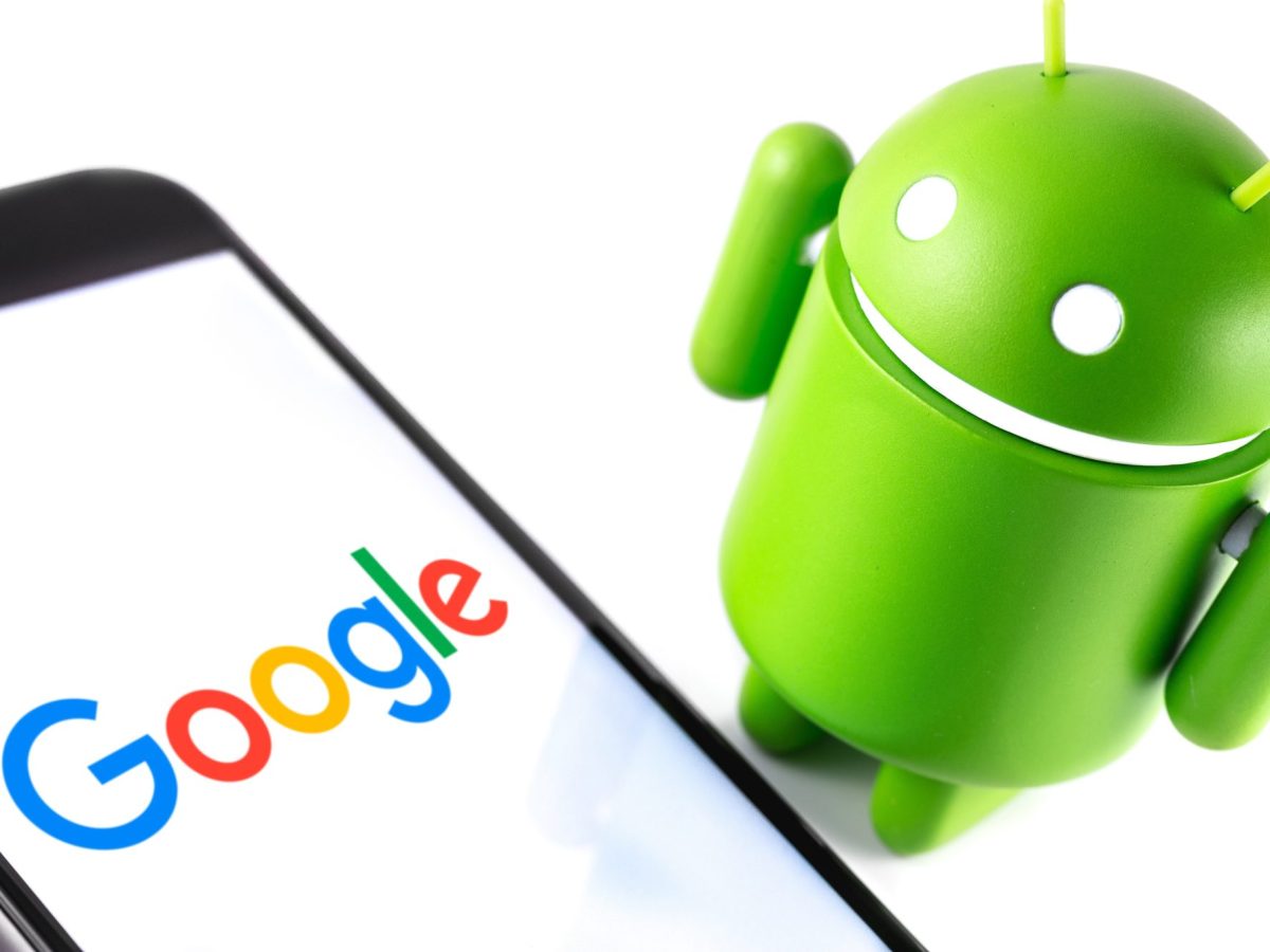 Android-Maskottchen steht neben einem Handy, auf dessen Bildschirm das Google-Logo zu sehen ist.