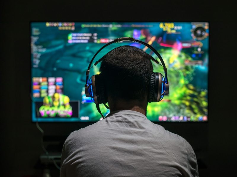 Gamer sitzt mit einem Headset auf dem Kopf vor einem Bildschirm, auf dem eine Spiel läuft.