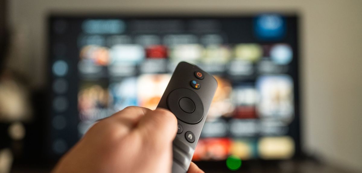 Person hält eine Fernbedienung auf einen eingeschalteten Fernseher