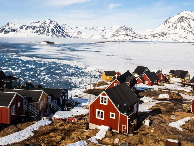 Eine Gemeinde in Grönland mit bunten Häuschen und einer Schneelandschaft im Hintergrund.