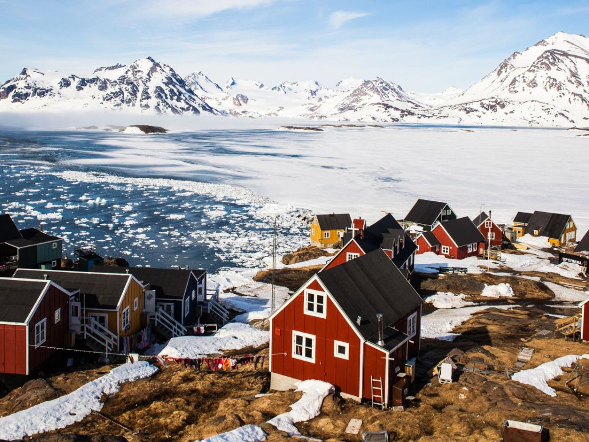 Eine Gemeinde in Grönland mit bunten Häuschen und einer Schneelandschaft im Hintergrund.