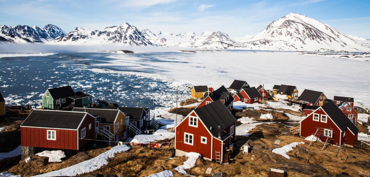 Eine Gemeinde in Grönland mit bunten Häuschen und einer Schneelandschaft im Hintergrund.