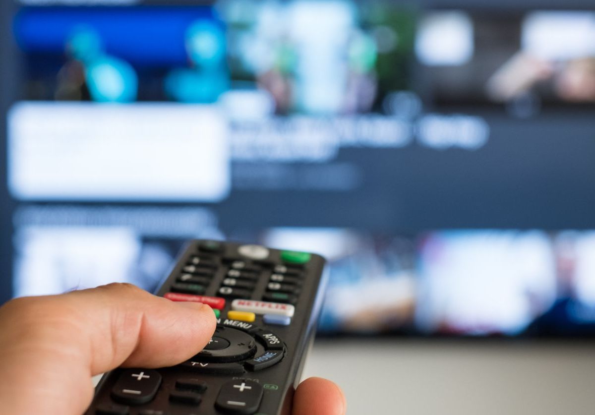 Unbekannte Person richtet Fernbedienung auf einen Fernseher.